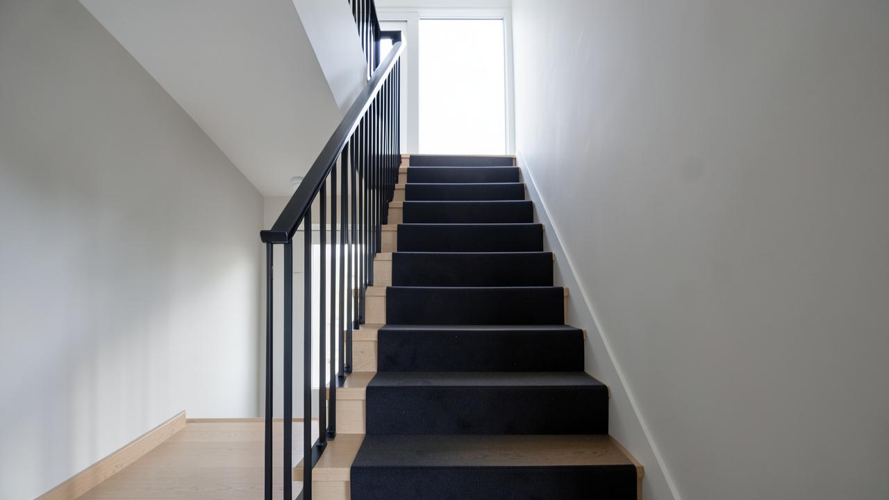 A contemporary staircase with a plain charcoal runner and black metal balustrade
